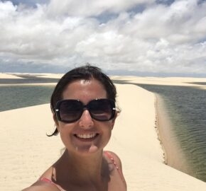 Person standing on sand dunes next to a water body under a cloudy sky.