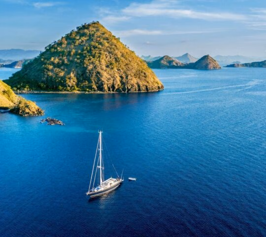 Sailboat with island under blue sky Aerial view of sailboat with island under blue sky in Labuan Bajo near Bali Island, Indonesia
