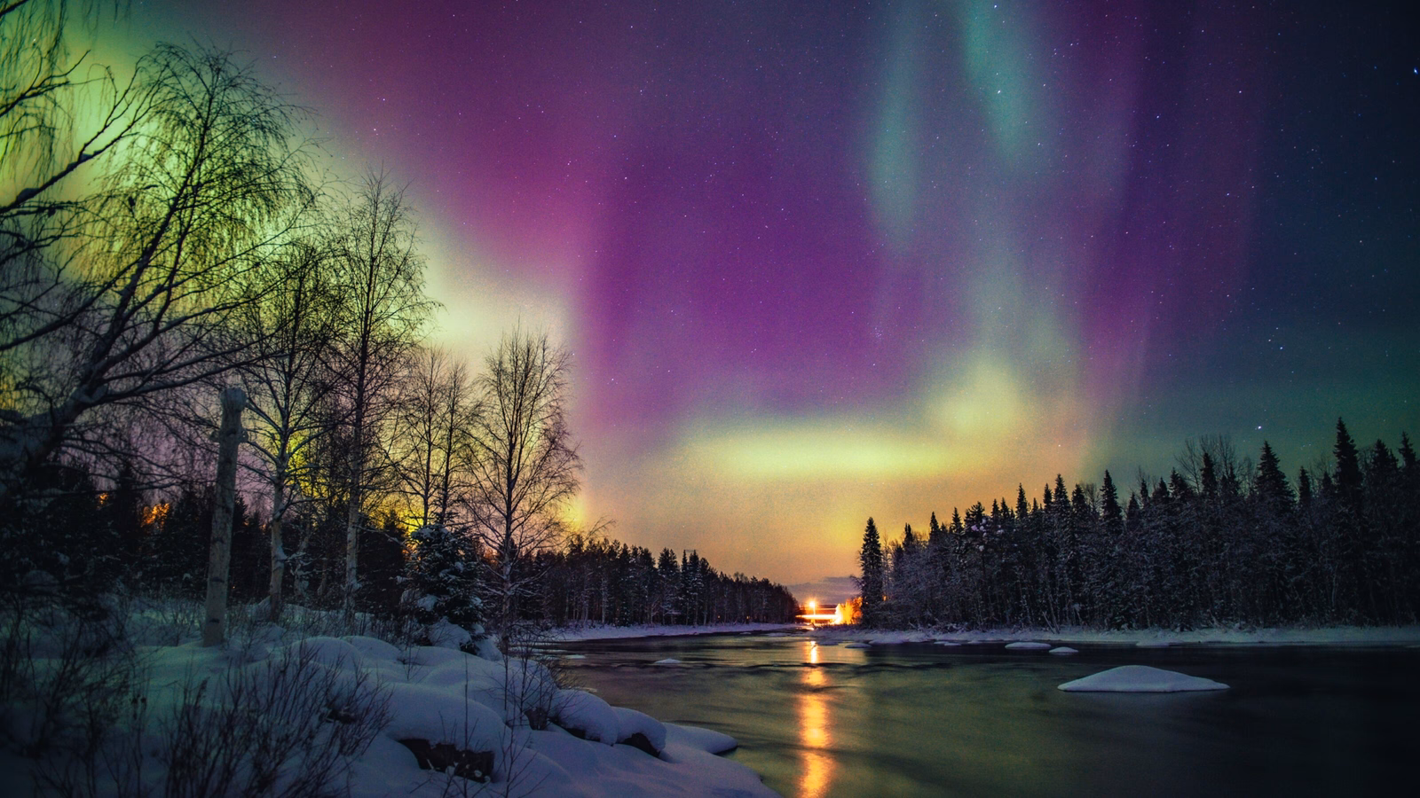 Aurora borealis over a snowy forest with a river reflecting colorful lights in the night.