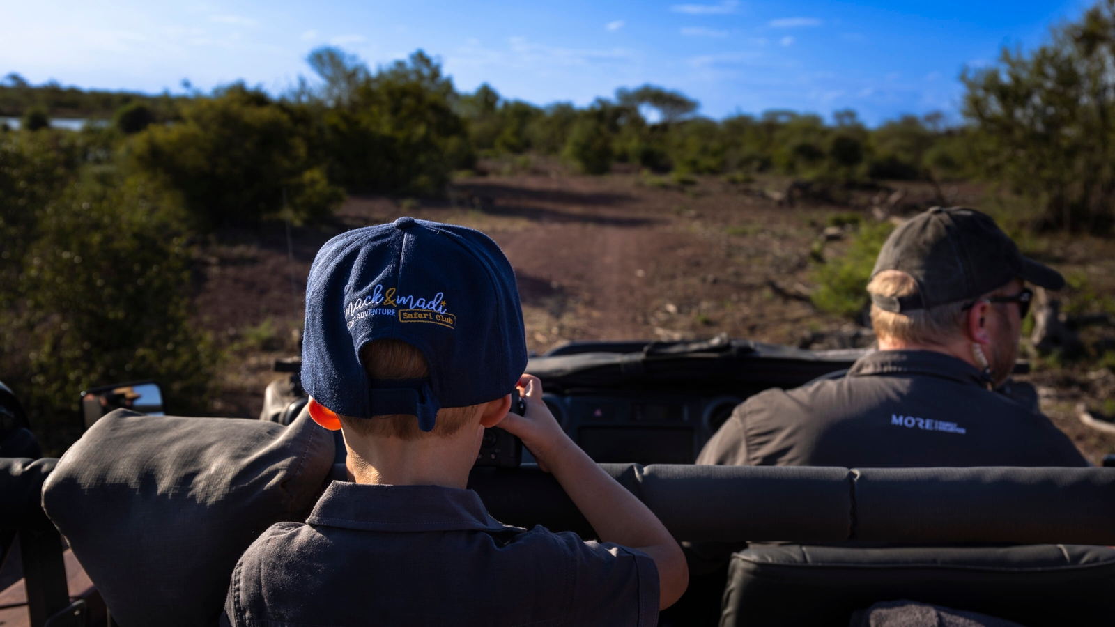Two people in a safari vehicle observing nature, one wearing a blue cap.