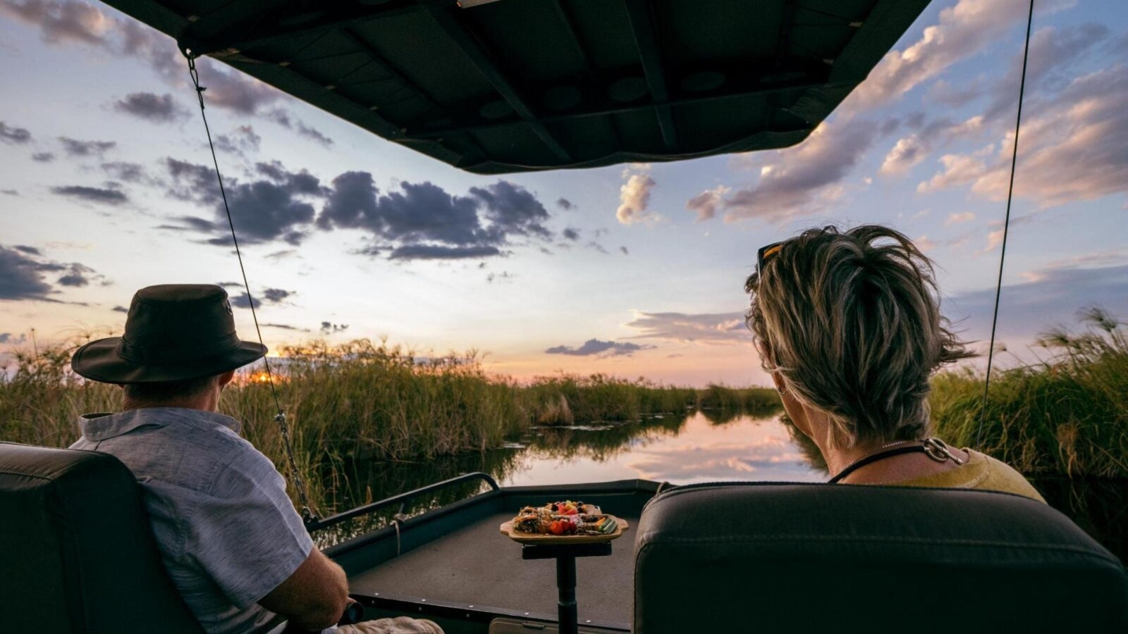 Two people watching a sunset from a boat with snacks on a table.