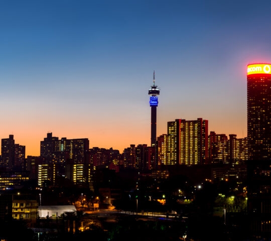 A city skyline at dusk with illuminated buildings and a tower.