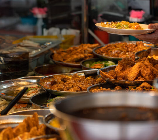 Person serving food at a buffet with various dishes in the foreground.