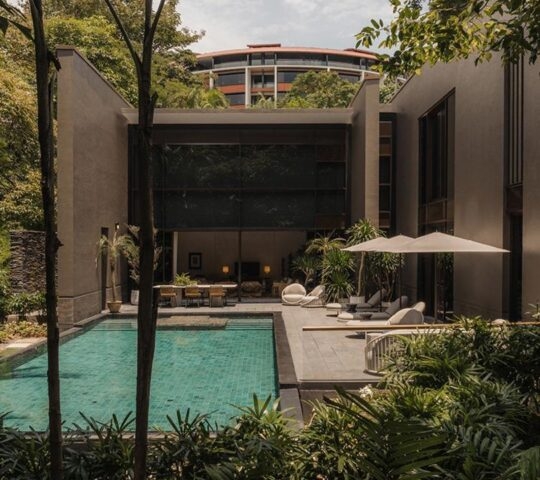 Modern house with pool surrounded by lush greenery and patio furnishings.