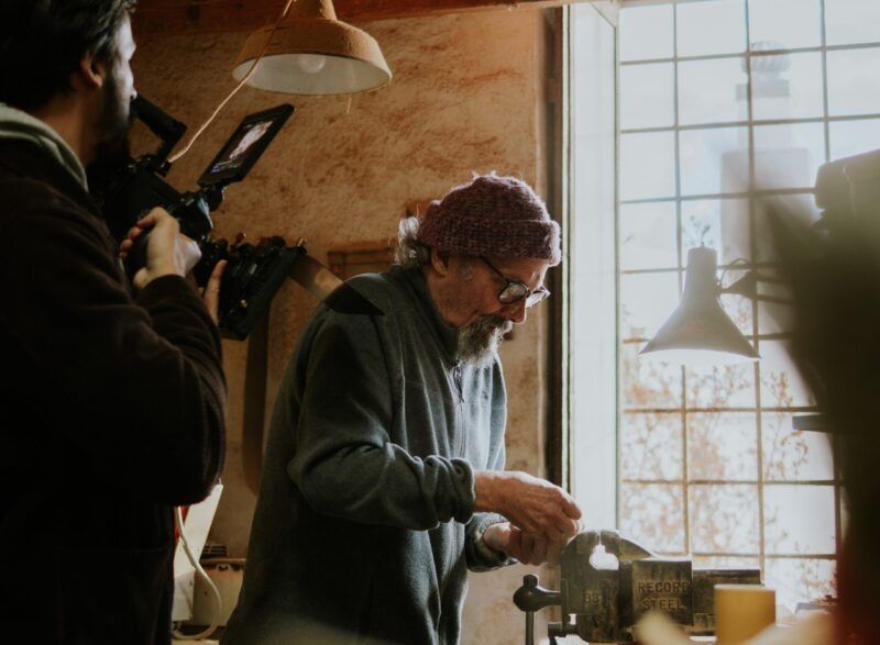 Person working in a workshop with filming equipment in the foreground.