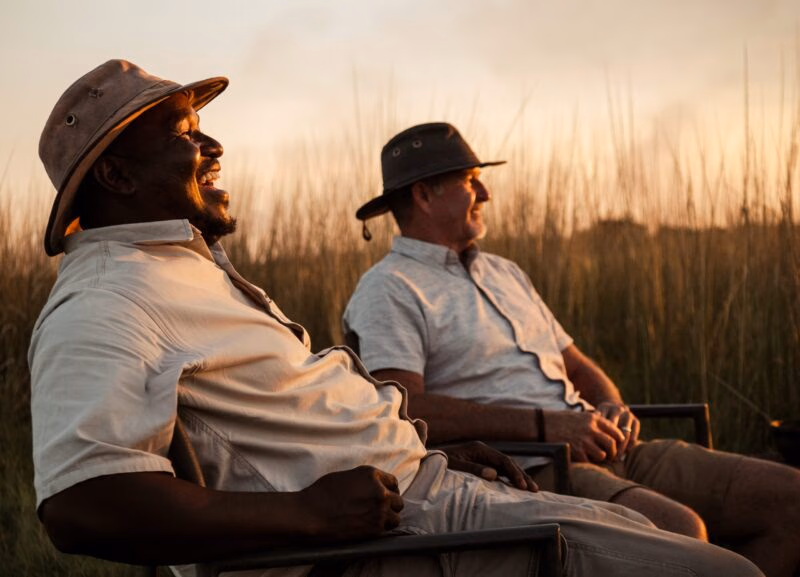 Two people sitting in chairs in a grassy field during sunset.