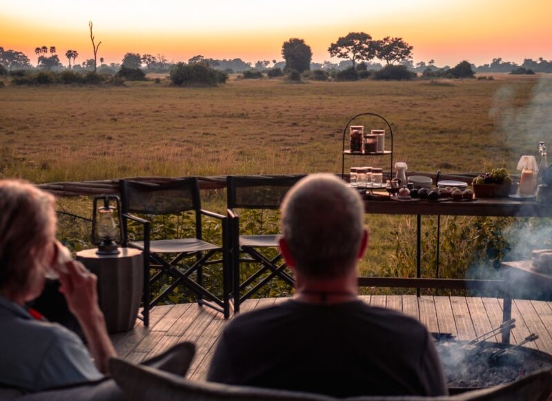 Two people enjoying a serene outdoor breakfast overlooking a grassy savanna at sunrise.