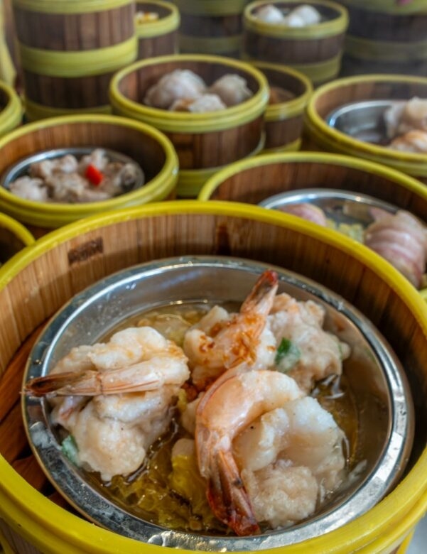 Dim sum dishes in steamer baskets, with a focus on shrimp dumplings in the foreground.