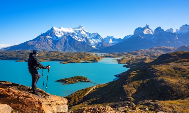Hiker overlooking a turquoise lake and mountain range.