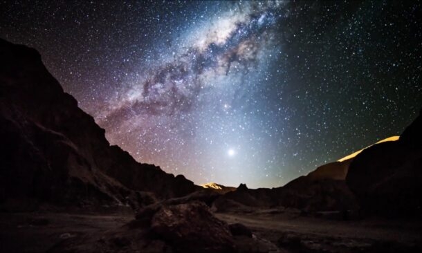 Starry night sky with the Milky Way over rugged terrain.