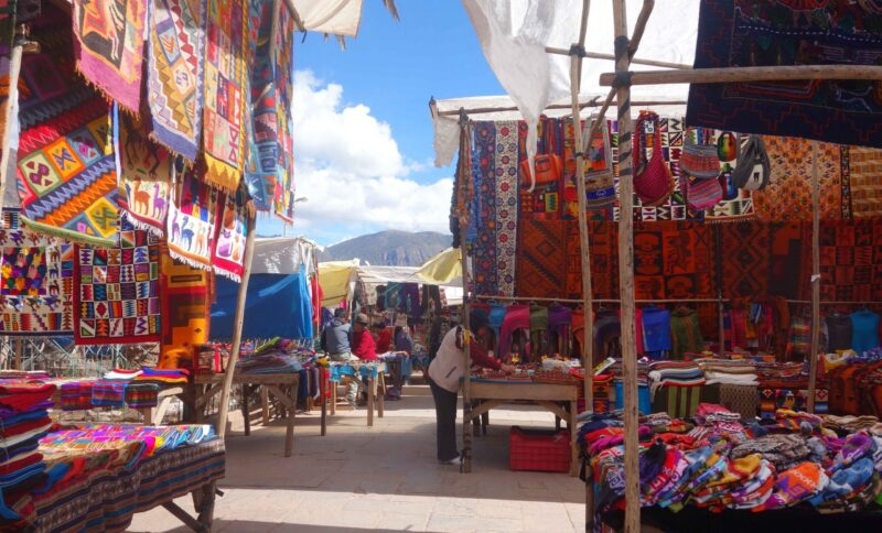 Colorful textile market stalls with hanging fabrics under a blue sky.