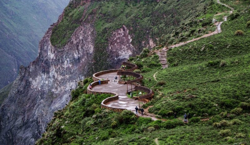 Winding mountain path with pedestrians and verdant slopes.