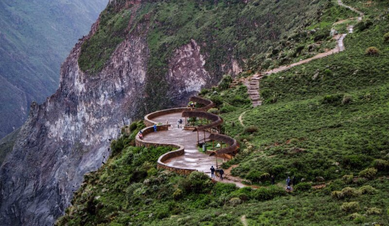 Winding mountain path with pedestrians and verdant slopes.