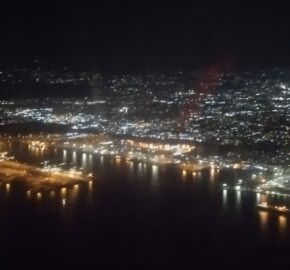 Aerial night view of a cityscape with lights reflecting on a body of water.