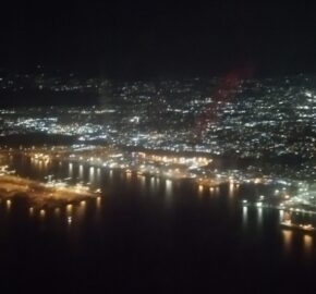 Aerial night view of a cityscape with lights reflecting on a body of water.