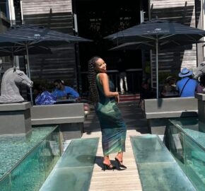 Person walking across a glass bridge with outdoor seating and umbrellas around.