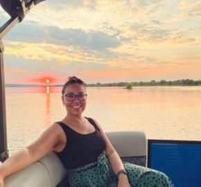 Person sitting on a boat at sunset over a serene lake with clouds in the sky.