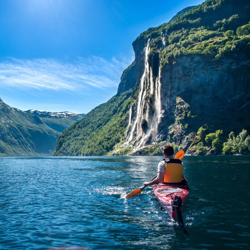 young man kayaking along the fjord geiranger enjoying the waterfall "seven sisters"
