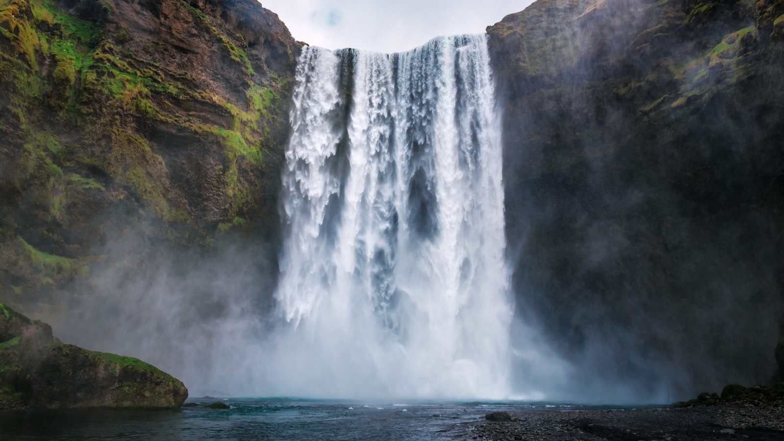Majestic waterfall cascading down mossy cliffs into a misty river below.