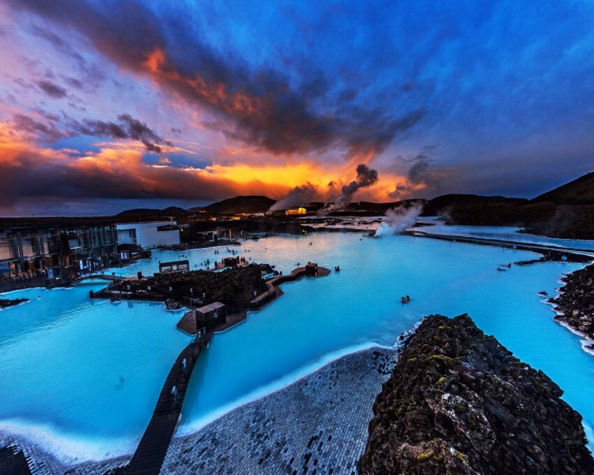 "Vibrant sunset over a milky-blue geothermal spa surrounded by volcanic rock formations."