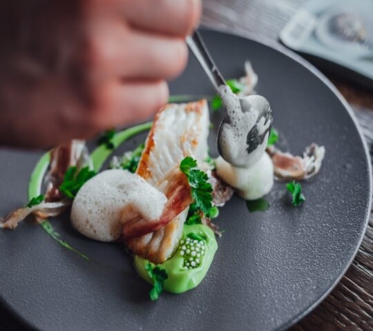 A gourmet dish with seafood and green sauce on a black plate.