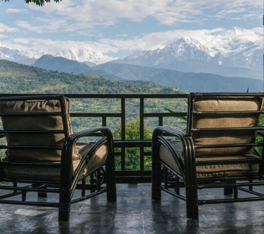 Two chairs on a balcony with a view of snow-capped mountains in the distance.
