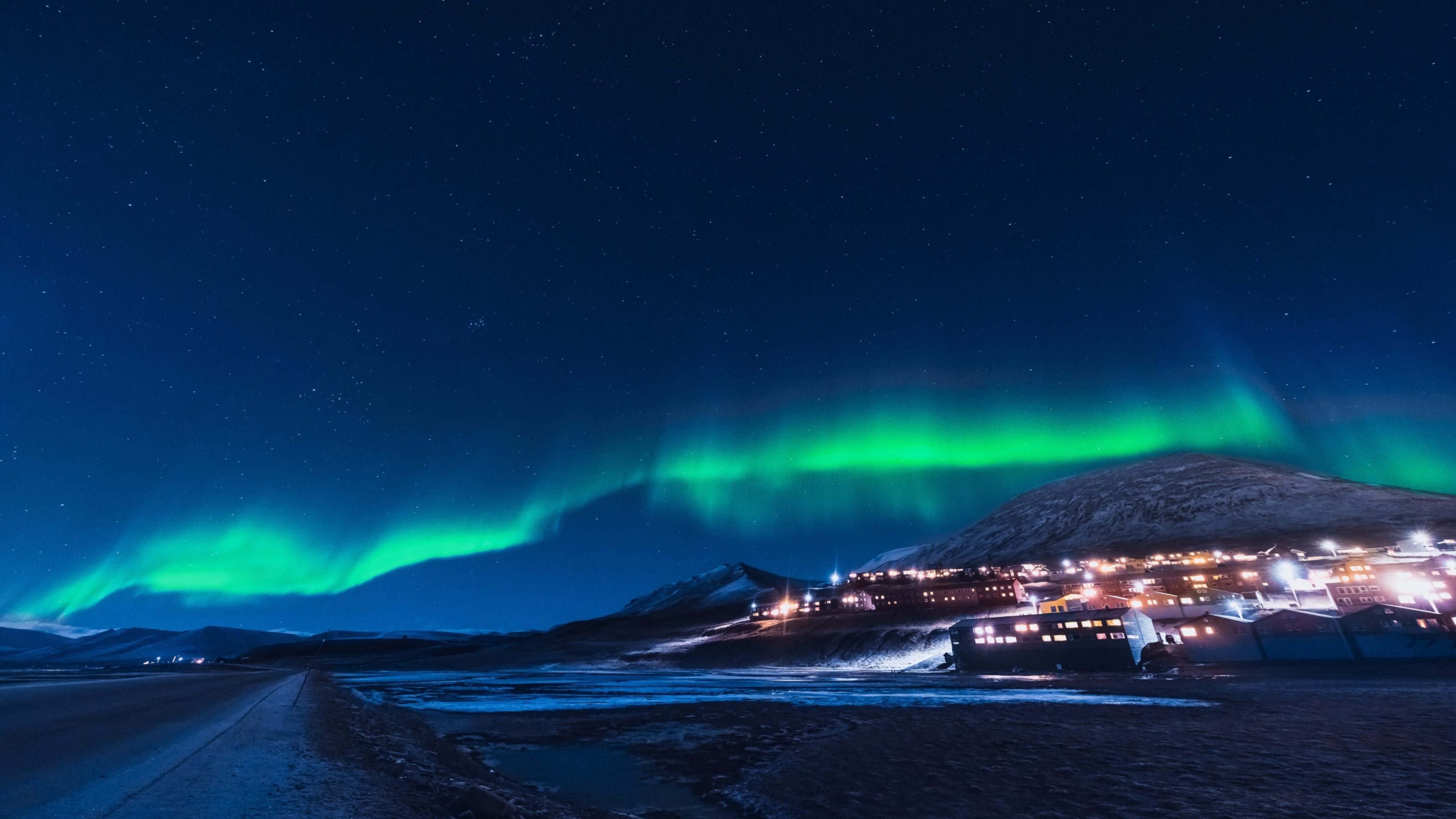 Aurora borealis over a snowy village with illuminated buildings at night.
