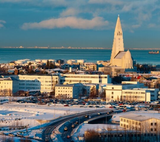 Snow-covered cityscape with a distinctive church spire during sunset.