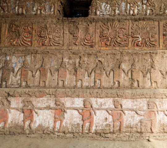 Ancient wall relief with rows of human and solar figures in earthy tones.