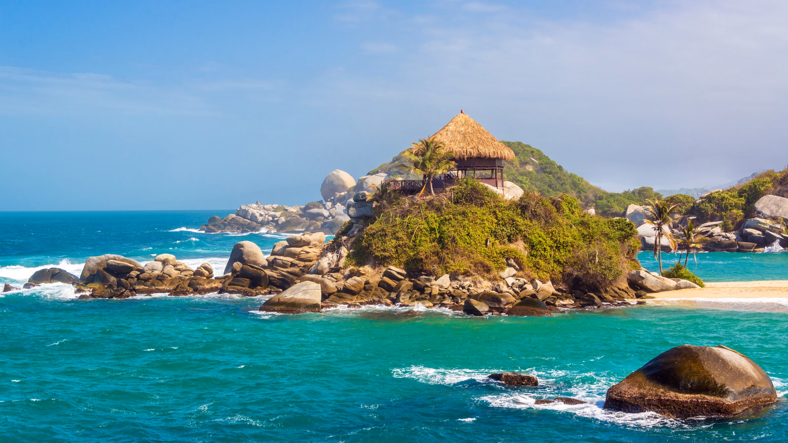 Thatched hut on a rocky island with lush greenery surrounded by turquoise sea.