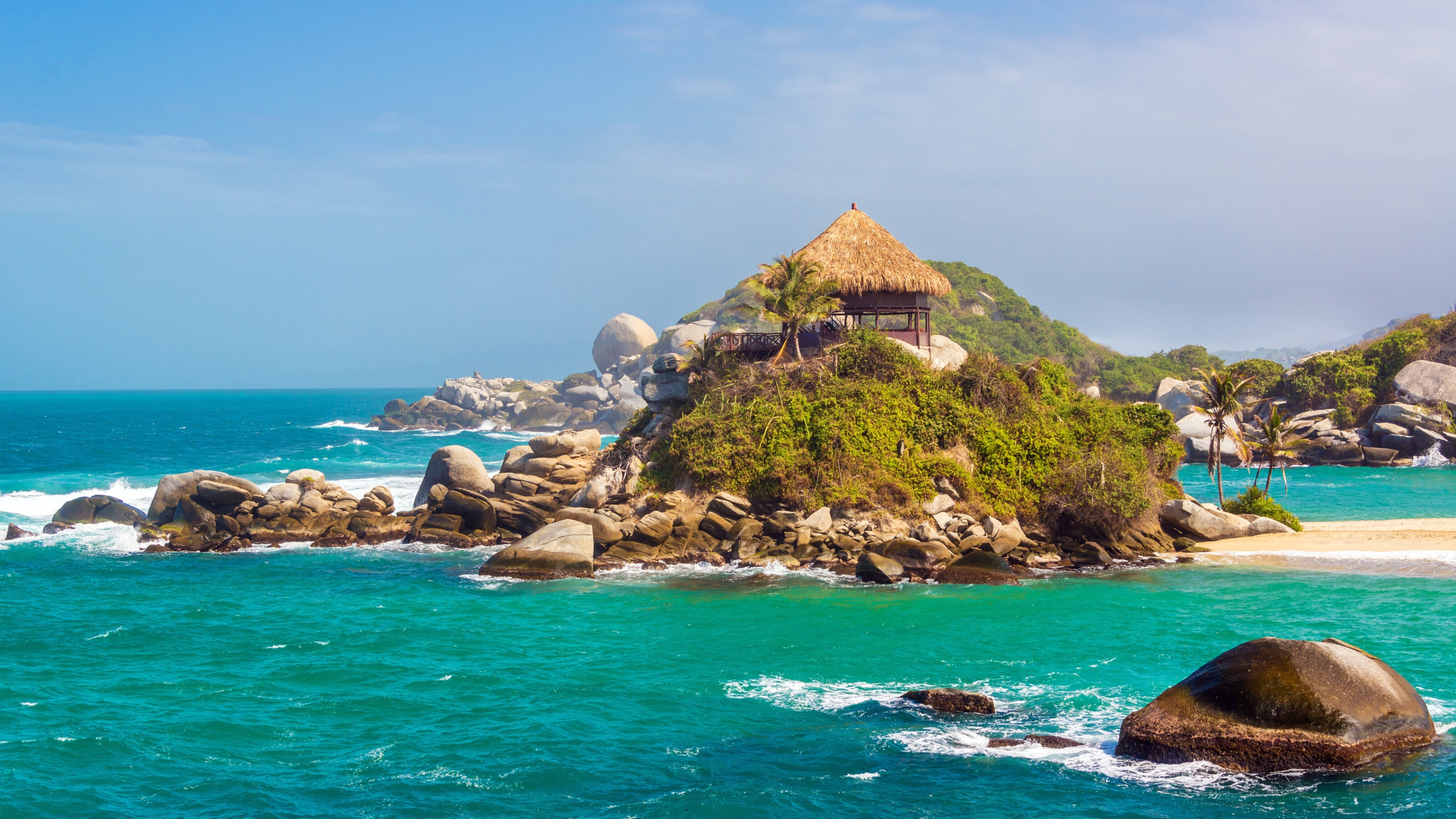 Thatched hut on a rocky island with lush greenery surrounded by turquoise sea.