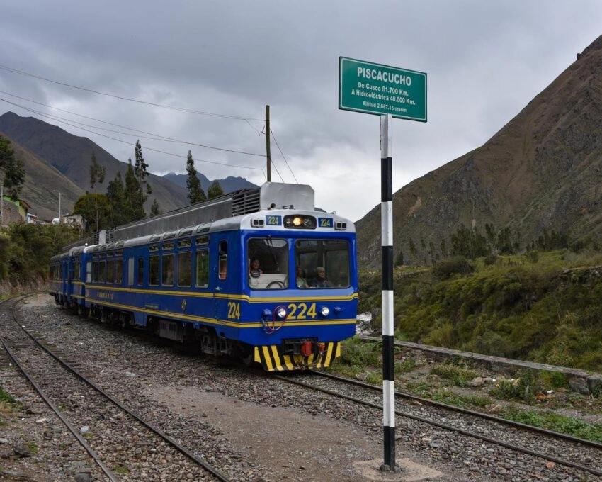 Blue train at Pisacucho station with mountainous background.