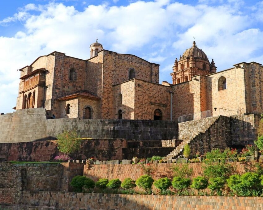 Historic stone church with a staircase and garden against a blue sky.
