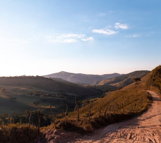 Dusty road winding through a hilly landscape at sunset with clear blue skies.