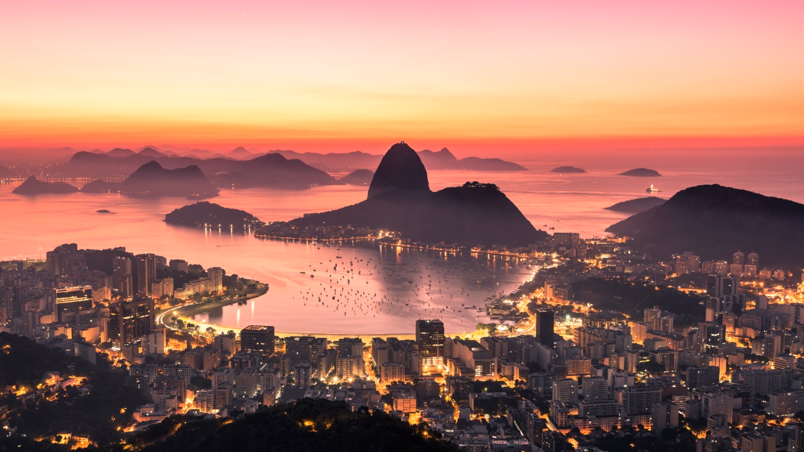 Aerial view of Rio de Janeiro at sunset with Sugarloaf Mountain and city lights.