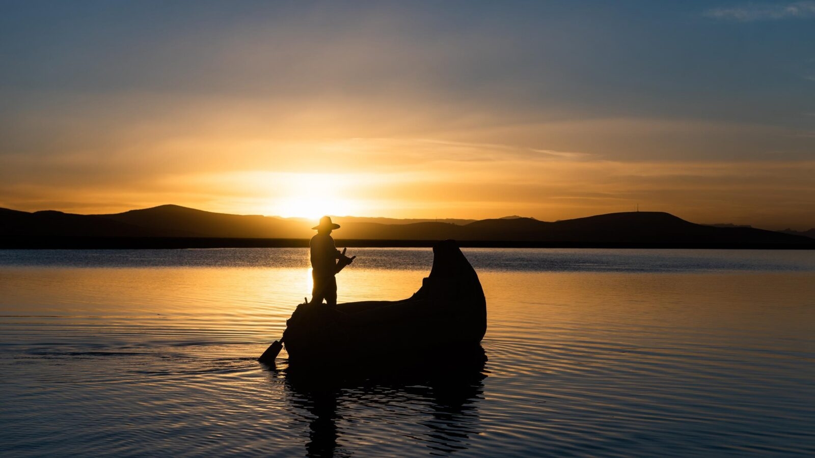 Man in traditional costume sailing in a traditional boat on lake titicaca at sunset puno peru