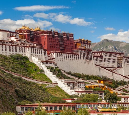 The Potala Palace in Lhasa, Tibet, against a backdrop of blue skies and mountains.