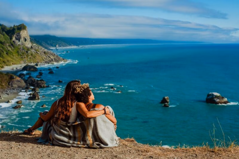 Couple sitting on the ground overlooking a beautiful coastline
