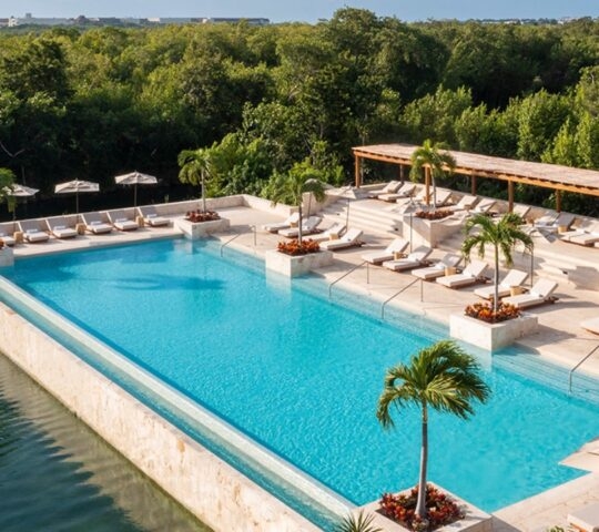 Luxury infinity pool with loungers and umbrellas overlooking lush greenery.