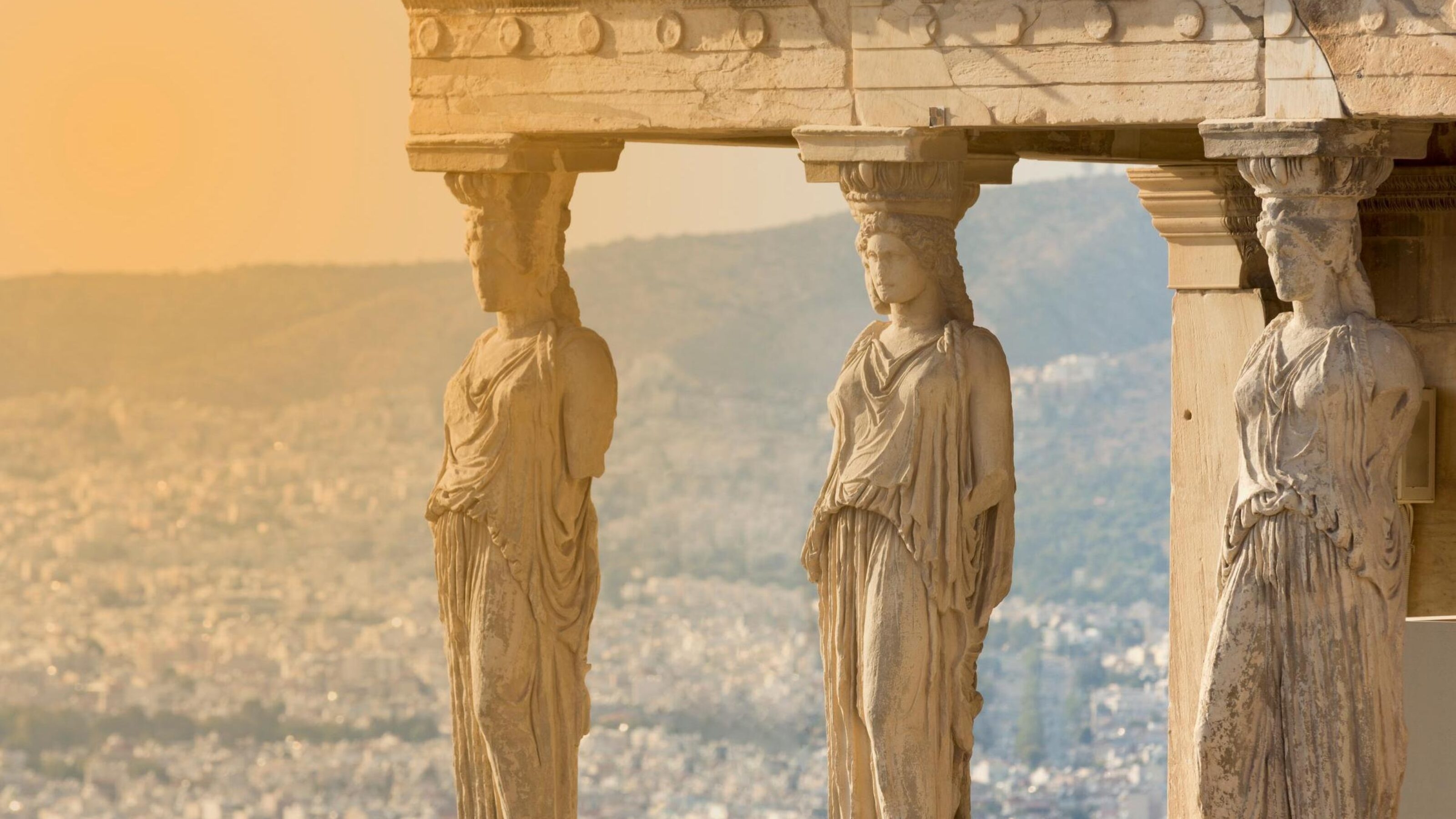 Ancient caryatid statues on a porch, overlooking a hilly landscape in golden light.