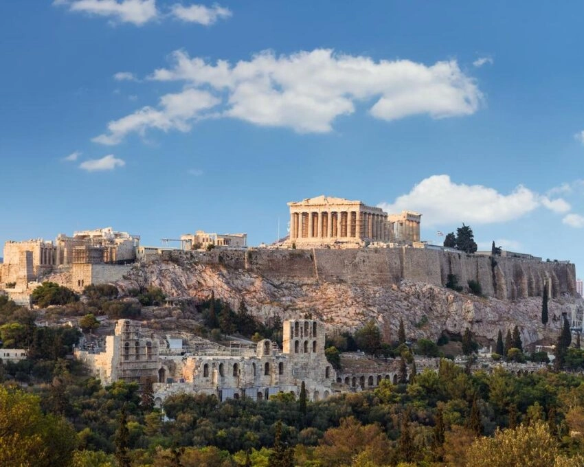 The Acropolis of Athens with the Parthenon at sunset under a blue sky with clouds.