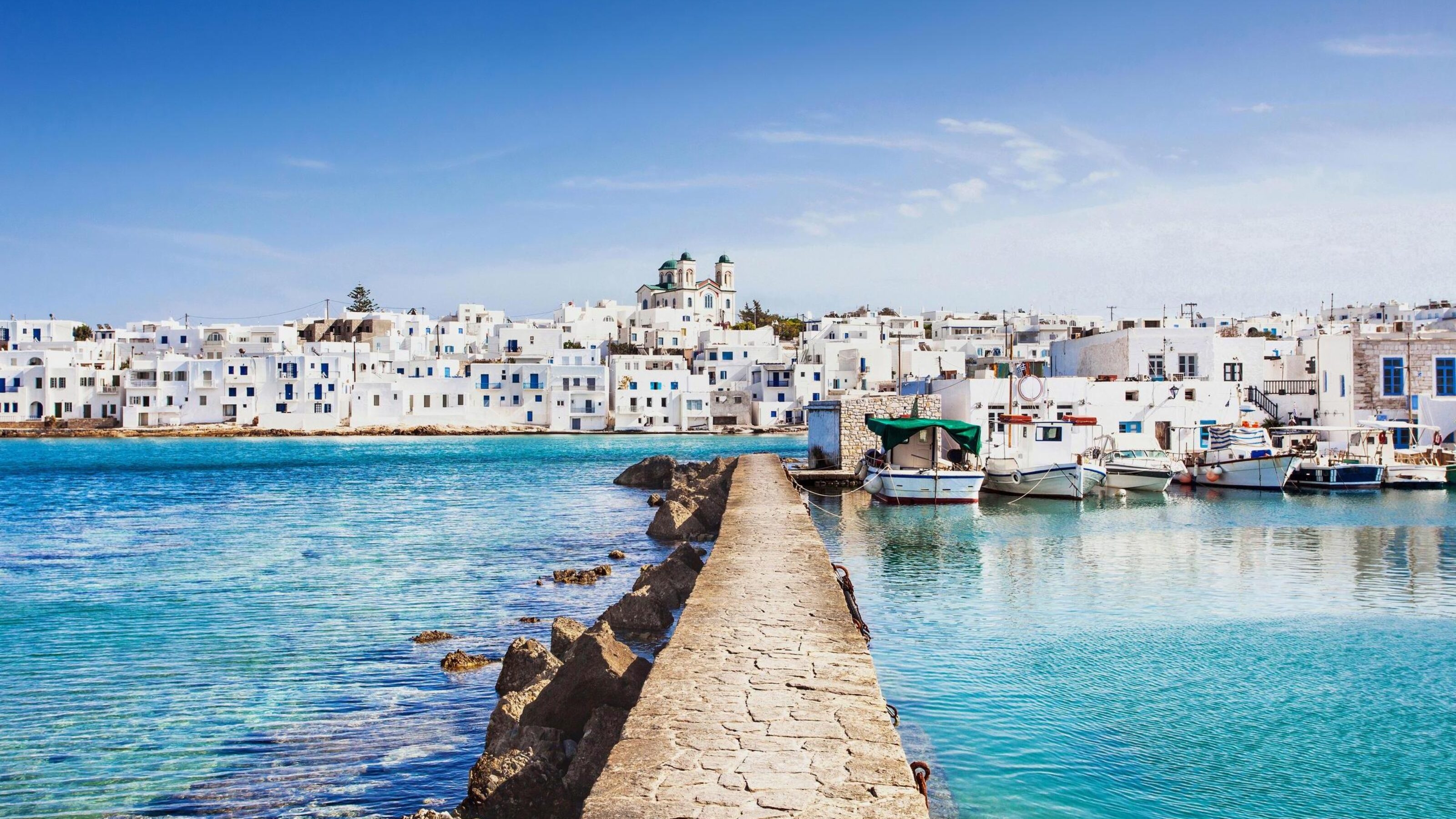 White buildings with blue domes in a Greek island town by the sea with moored boats.