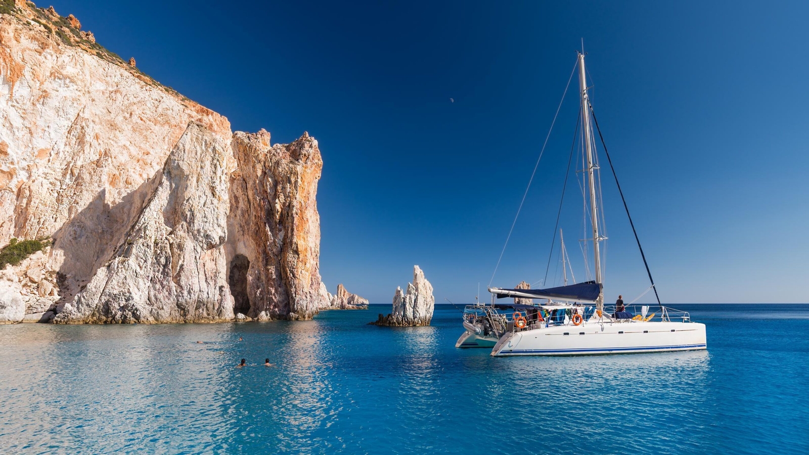 A boat anchored next to a rocky outcrop in Milos, Greece