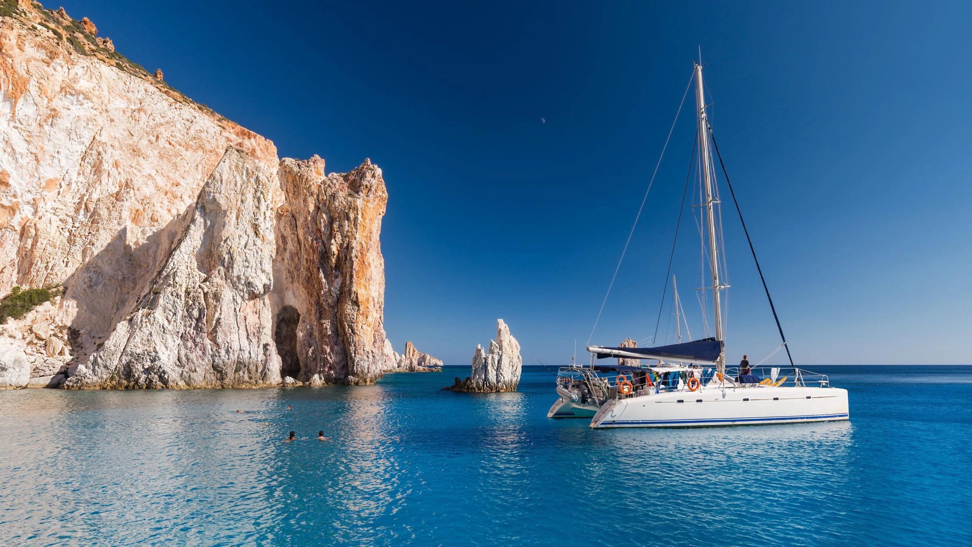 A boat anchored next to a rocky outcrop in Milos, Greece