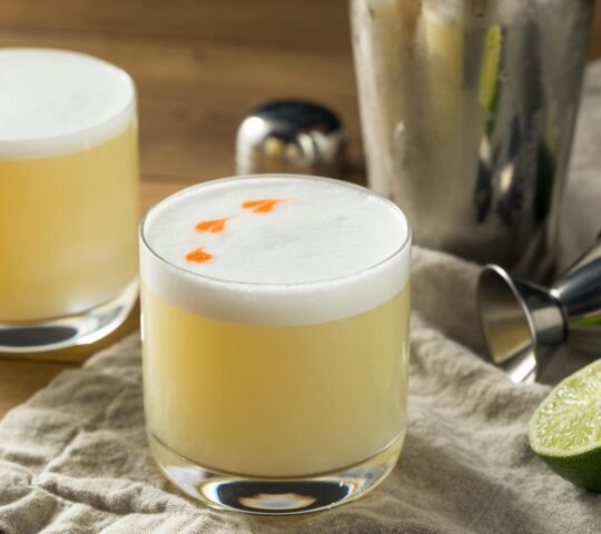 A pisco sour with cocktail making equipment in the background