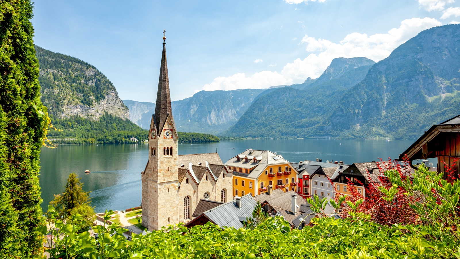 A picturesque village with colorful houses and a church by a lake, against a backdrop of mountains.