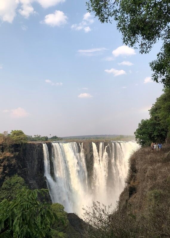 Majestic waterfall with mist and a rainbow, surrounded by greenery and cliffs.