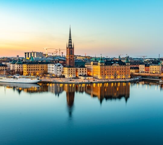 Twilight cityscape with historic buildings reflected in calm water.