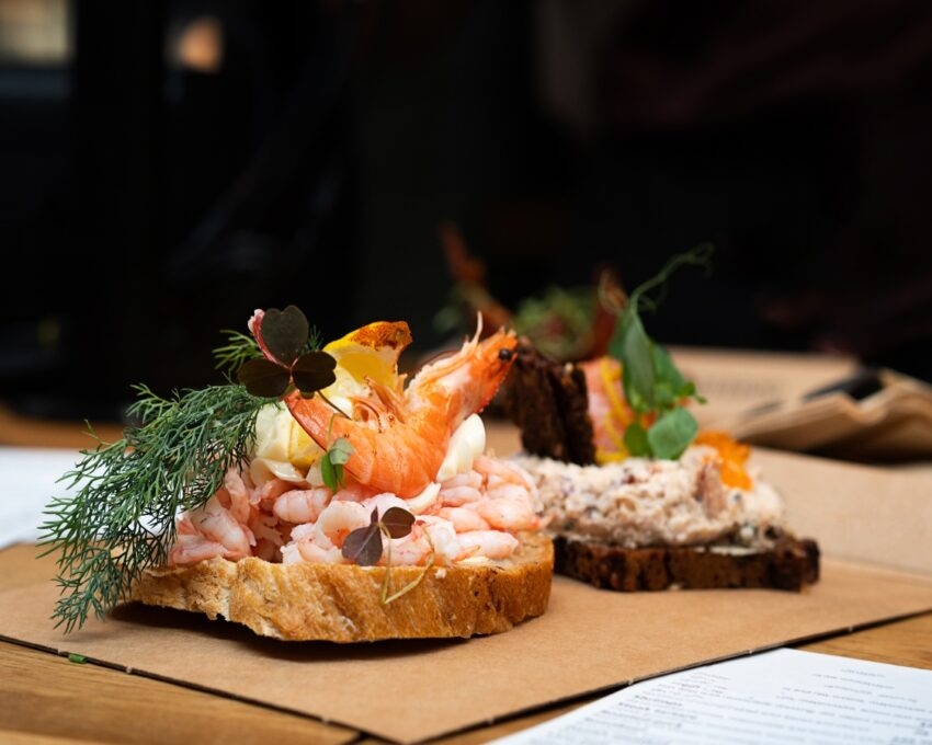 Open-faced shrimp sandwiches garnished with herbs on a paper-lined table.