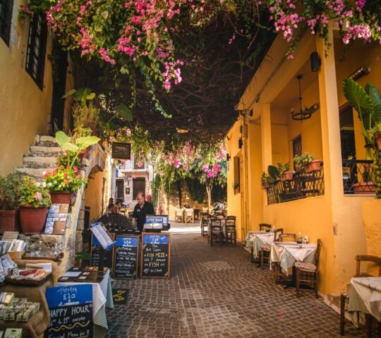 Charming alleyway with outdoor seating, cobblestones, and pink flowers.
